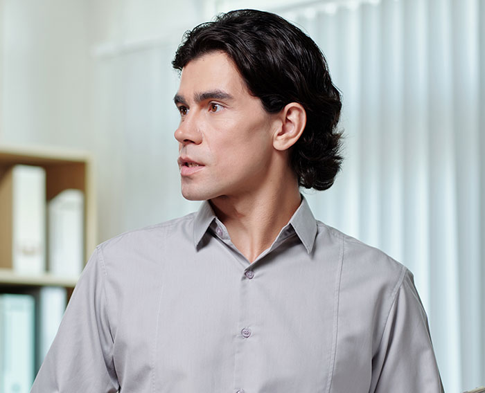 Man in gray shirt looking to the side with serious expression, illustrating CFO firing employee after body-shaming comment Man in gray shirt looking to the side with serious expression, illustrating CFO firing employee after body-shaming comment