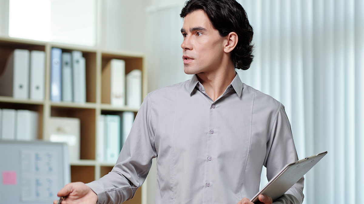 Young professional man in gray shirt holding clipboard in office, reacting to termination after body-shaming comment discussion