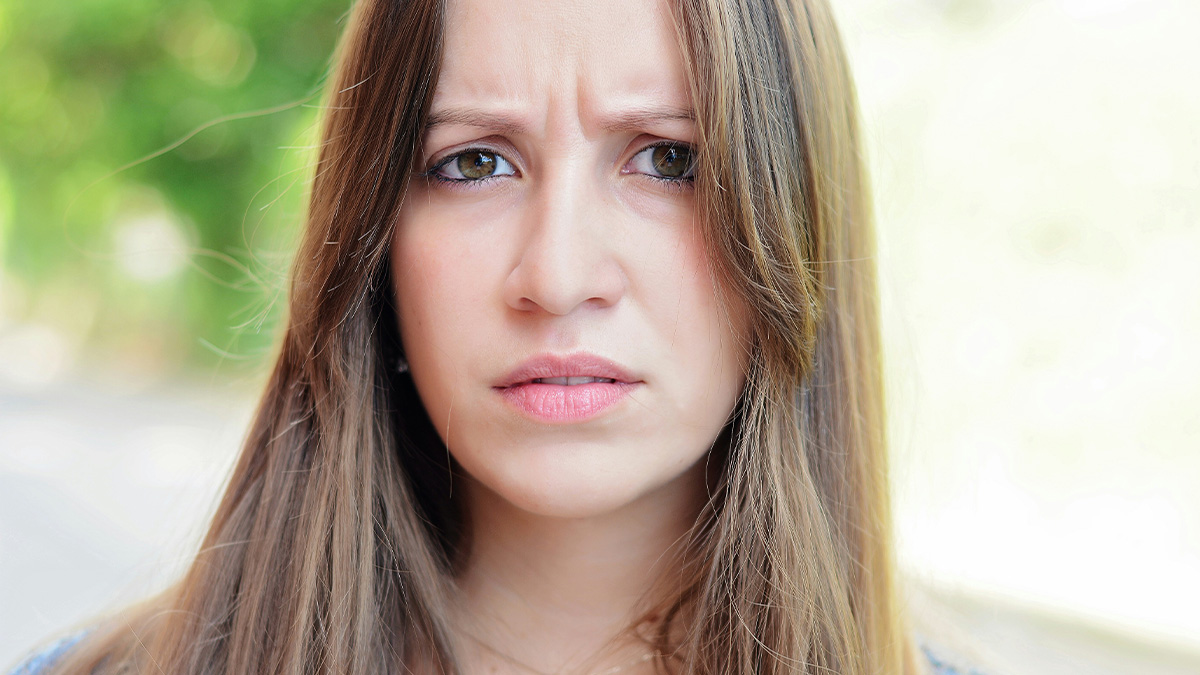 Young woman with long hair looking worried and regretful outdoors, reflecting on mortgage and roommate issues.