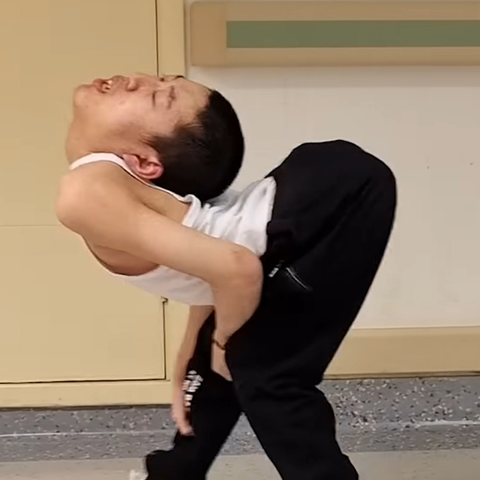 Boy known as folded boy bending his body backwards at an extreme angle indoors against a plain background Boy known as folded boy bending his body backwards at an extreme angle indoors against a plain background