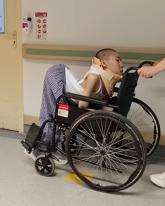 Young folded boy bent at 180 degrees in a wheelchair receiving help inside a medical facility hallway. Young folded boy bent at 180 degrees in a wheelchair receiving help inside a medical facility hallway.