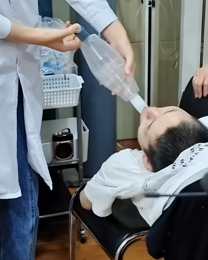 Boy bent at 180 degrees receiving medical care, lying on chair with breathing assistance from healthcare worker. Boy bent at 180 degrees receiving medical care, lying on chair with breathing assistance from healthcare worker.