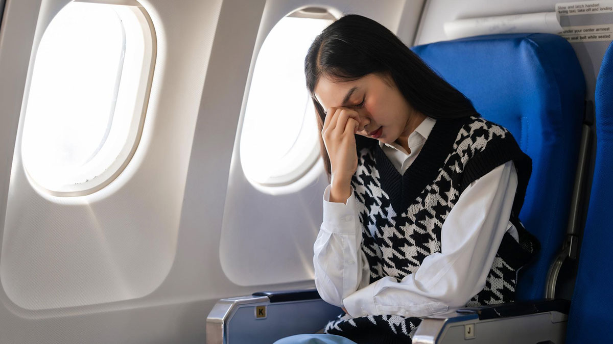 Woman on airplane frustrated and stressed in seat, reflecting tension over armrest and obese passenger issue.