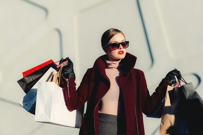 Woman in sunglasses and stylish coat holding multiple shopping bags representing overhyped products people should stop buying.