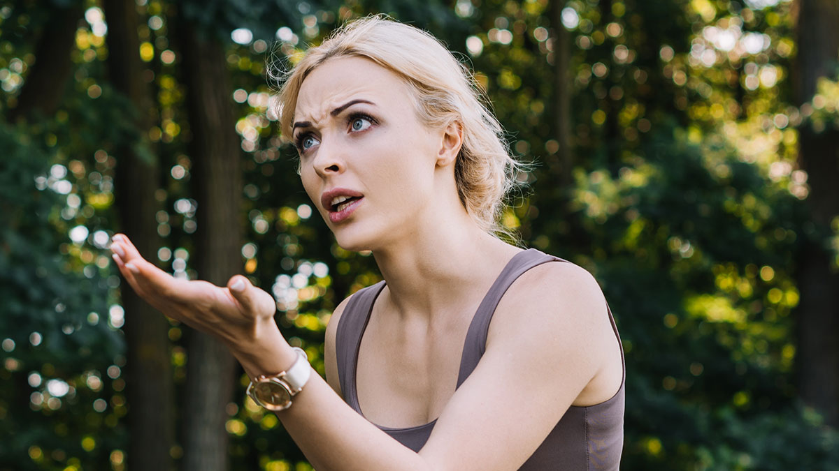 British woman showing frustration outdoors, reacting to parenting lecture from French shop owner on holiday trip.