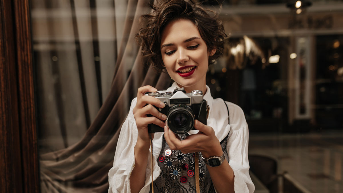 Young woman smiling while holding a vintage camera, relating to friend stealing boyfriendu2019s camera confrontation story.