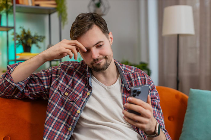 Man in plaid shirt looking at phone with concerned expression, reflecting on groom kissing best friend at bachelor party. Man in plaid shirt looking at phone with concerned expression, reflecting on groom kissing best friend at bachelor party.