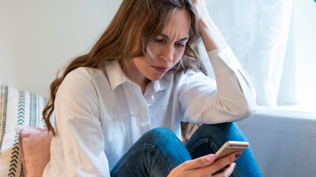 Young woman looking upset while checking phone, illustrating friend group cancels weekend getaway plans.