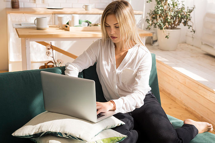 Young woman using a laptop on a couch in a bright room, reflecting on sister unwanted siblings adoption topics. Young woman using a laptop on a couch in a bright room, reflecting on sister unwanted siblings adoption topics.