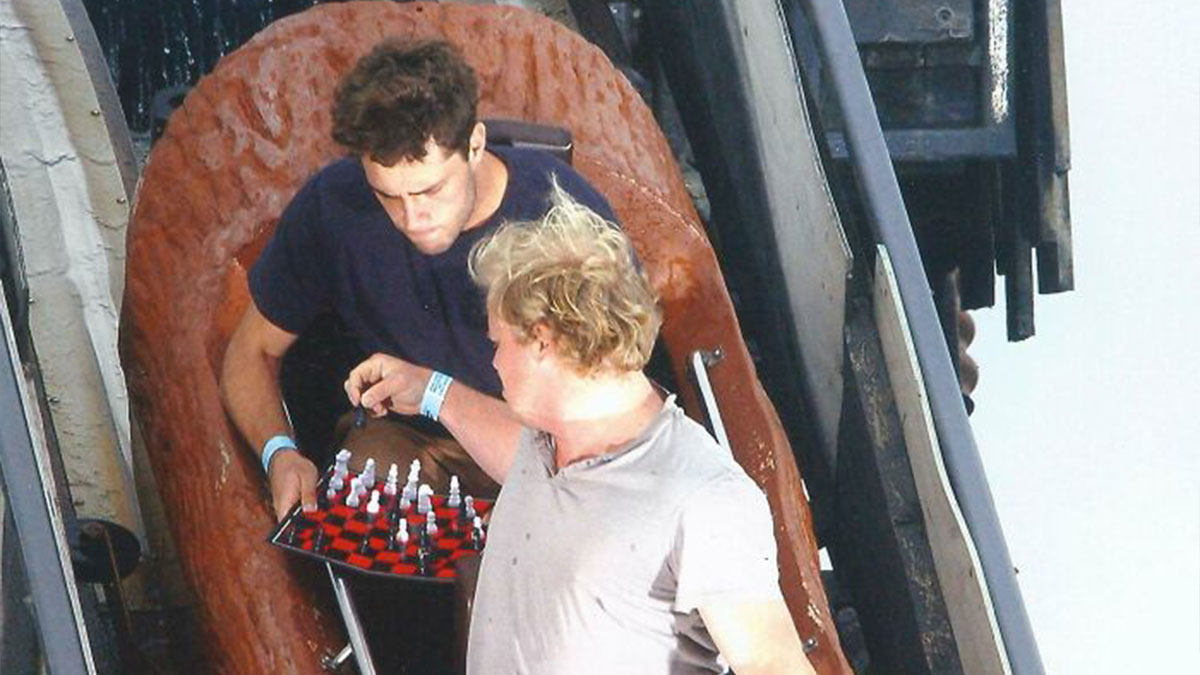 Two men playing chess on a board while riding a log flume at an amusement park capturing a unique photo moment.
