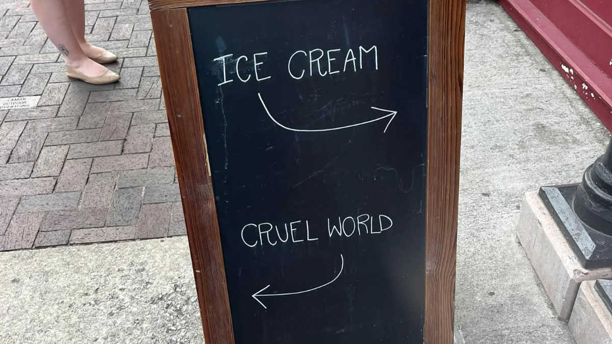 Sidewalk chalkboard sign humorously contrasting ice cream and the cruel world, fitting funny and bizarre images theme.