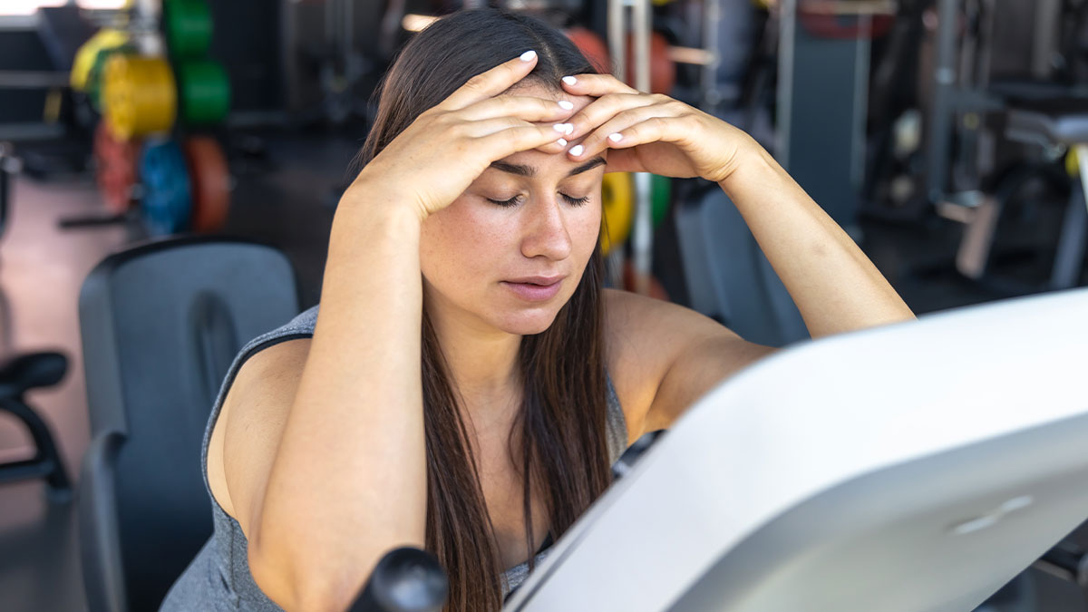 Woman looking stressed on gym equipment, illustrating challenges of fitness influencers taking baby to the gym.
