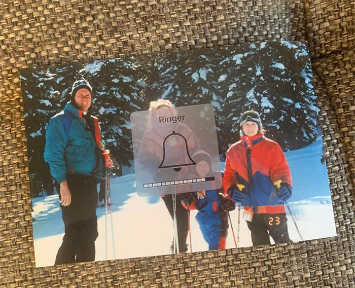 Older people failing at technology shown by photo volume control overlay blocking family ski photo on phone screen.