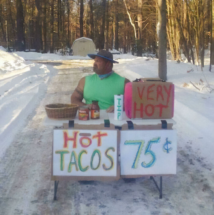 Man in a green shirt with funny parents selling hot tacos for 75 cents on a snowy road in winter woods.