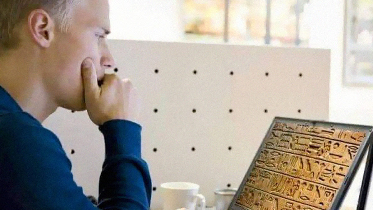Programmer with a blue shirt studying ancient hieroglyphics displayed on a laptop screen in a modern workspace.