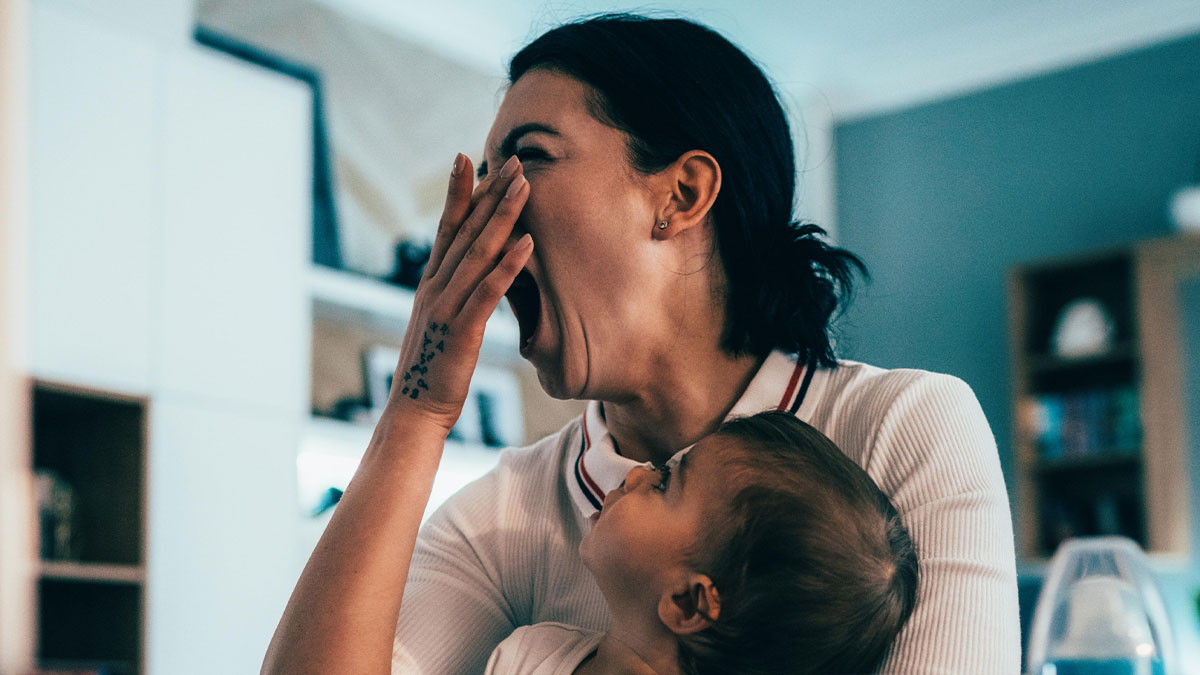 Tired parent holding baby yawning in a cozy home setting showing real moments of parenting life.