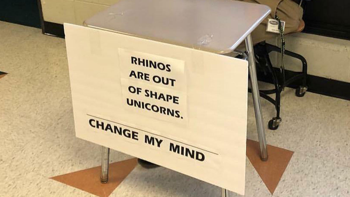 Humorous teacher desk with a sign challenging students about rhinos and unicorns, showcasing funny teacher humor.