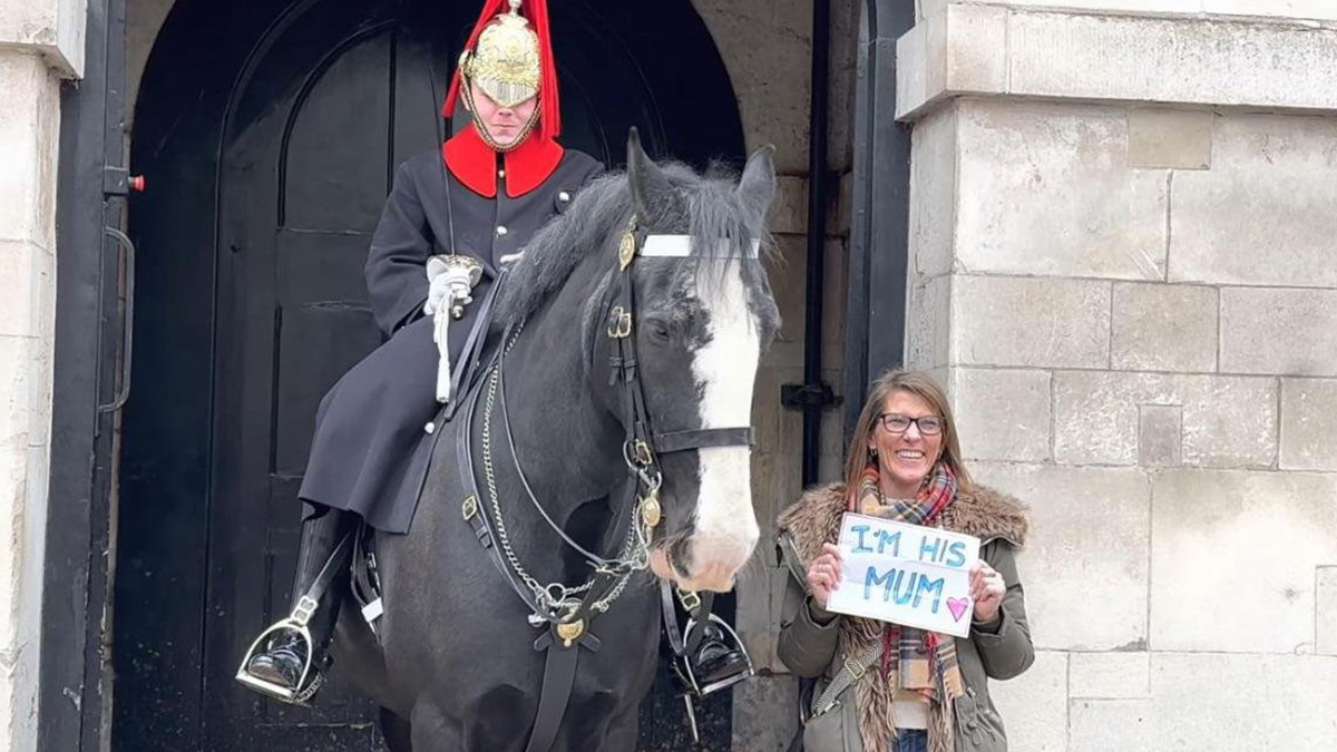 Smiling mom holding a sign next to a mounted guard in uniform, capturing an amazing wholesome moment.
