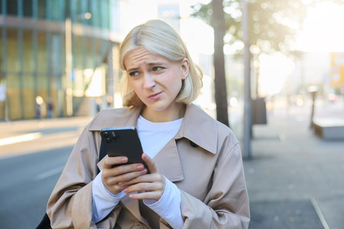 Woman outdoors looking confused while holding smartphone, illustrating entitled neighbor conflict and towing dispute. Woman outdoors looking confused while holding smartphone, illustrating entitled neighbor conflict and towing dispute.