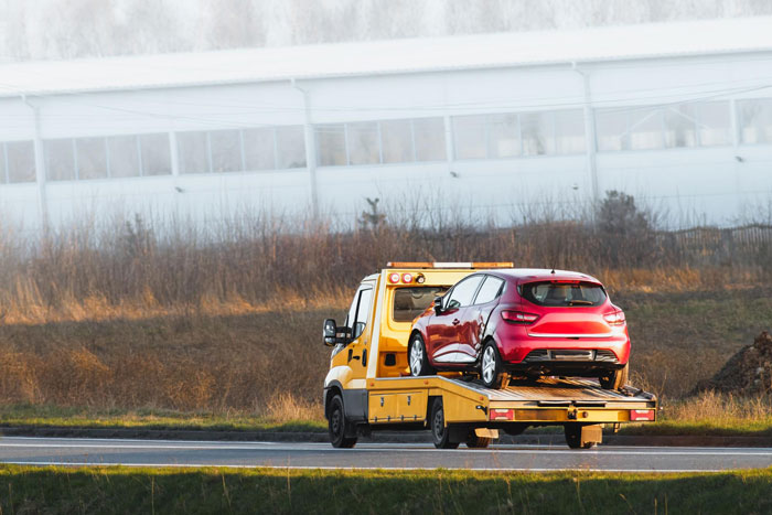 Yellow tow truck carrying red car on highway, illustrating man tows entitled neighbor’s car after blocking his vehicle. Yellow tow truck carrying red car on highway, illustrating man tows entitled neighbor’s car after blocking his vehicle.