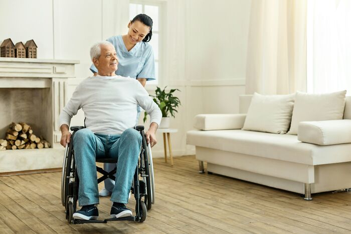 Elderly man in wheelchair with caregiver in a bright living room, illustrating folks who drained their savings.