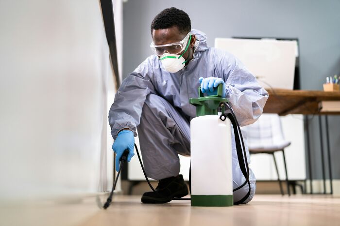 Man in protective gear using a sprayer for pest control indoors, highlighting suspicious professions like butcher and gravedigger.