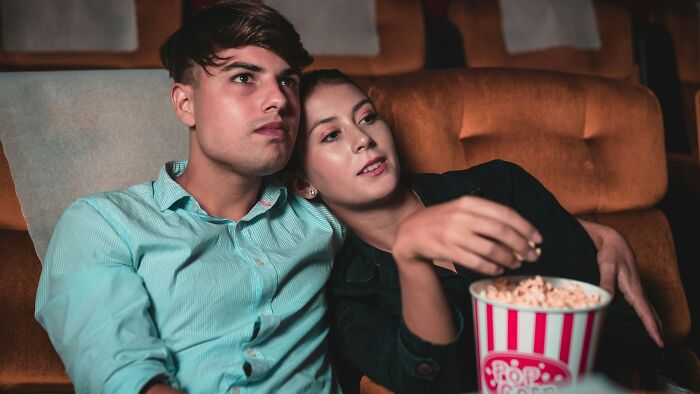 A young couple sitting close in a theater, sharing popcorn, illustrating childish reasons ladies ditched a guy.