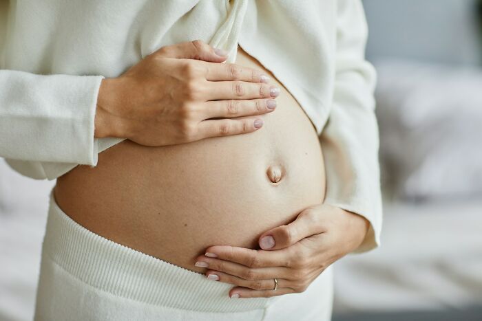 Close-up of a pregnant woman gently holding her belly in a soft cozy setting representing out of touch moments.