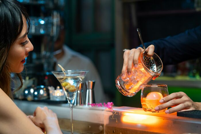 Bartender preparing a cocktail at a bar, with a woman watching, highlighting professions that raise suspicion when combined.