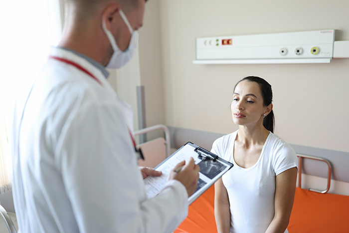 Doctor in a medical mask reviews patient notes with a woman in a white shirt during a consultation about infections. Doctor in a medical mask reviews patient notes with a woman in a white shirt during a consultation about infections.
