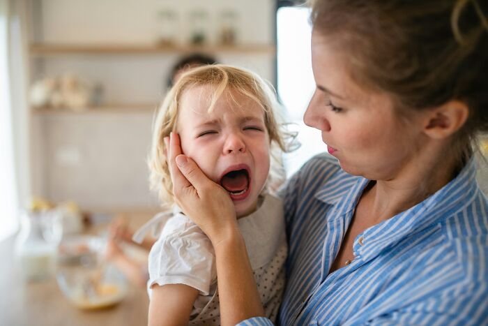 Mother comforting a crying toddler in a bright kitchen, illustrating parenting hacks that help save sanity during stressful moments.