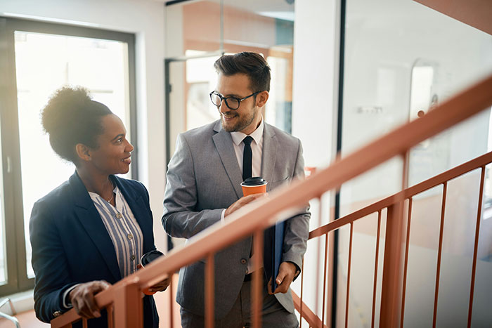 Two coworkers in business attire having a casual conversation indoors, illustrating creepy coworker petty response concept. Two coworkers in business attire having a casual conversation indoors, illustrating creepy coworker petty response concept.