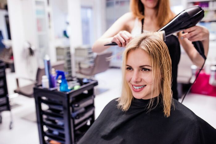 Young woman smiling while getting her hair blow-dried at a salon, illustrating opinions on kaomojis cultural appropriation.