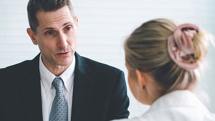 Man in suit speaking seriously to coworker with hair in bun, illustrating creepy coworker petty response in office setting. Man in suit speaking seriously to coworker with hair in bun, illustrating creepy coworker petty response in office setting.