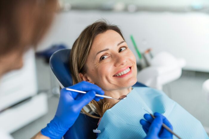 A smiling woman receiving dental care from a professional wearing blue gloves, highlighting suspicious profession combinations.