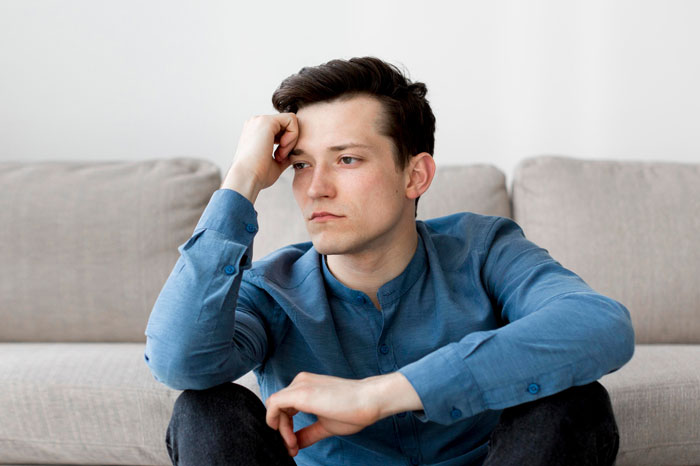 Young man looking frustrated and thoughtful while sitting on the floor in a living room setting. Young man looking frustrated and thoughtful while sitting on the floor in a living room setting.