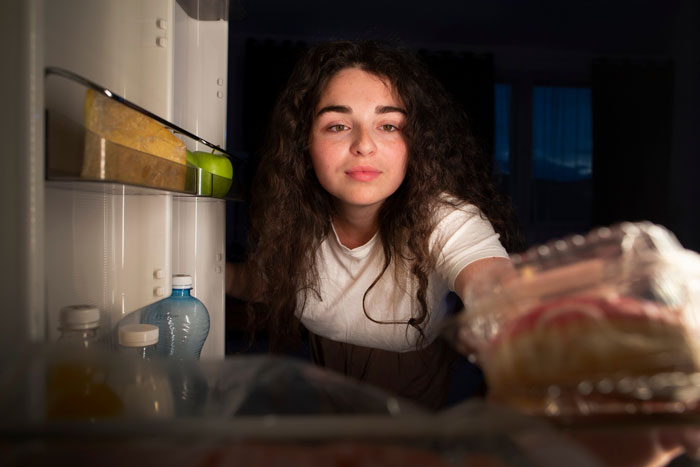 Young woman looking into fridge at night, upset about bro’s girlfriend eating food causing drama at home. Young woman looking into fridge at night, upset about bro’s girlfriend eating food causing drama at home.