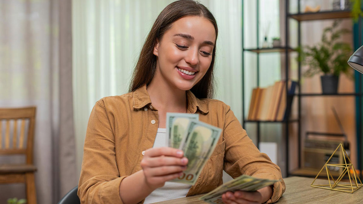 Young woman smiling while counting money at home, representing girlfriend wants to quit job after winning lottery.