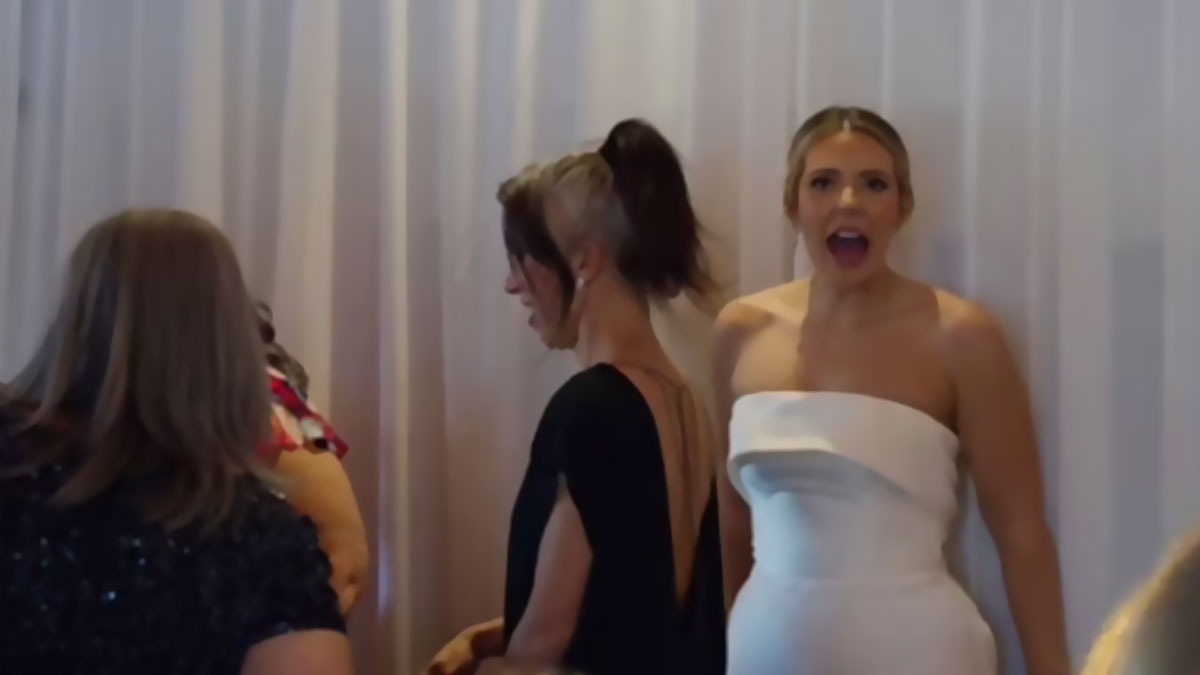 Woman in white dress at event, surrounded by guests, considering recreating wedding photos due to bad originals