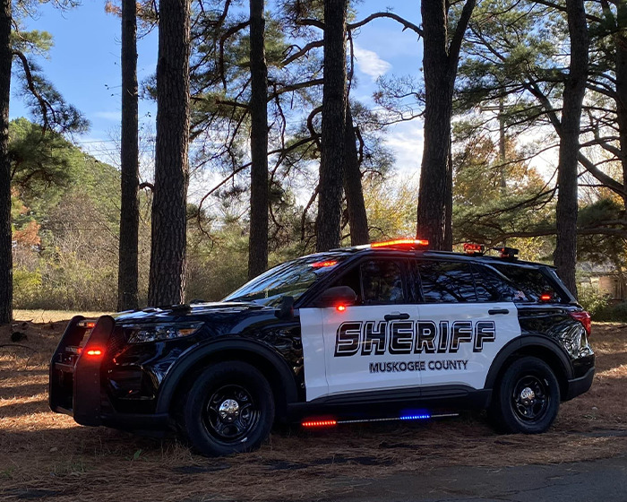 Muskogee County sheriff vehicle parked in a wooded area with lights flashing during an ongoing investigation. Muskogee County sheriff vehicle parked in a wooded area with lights flashing during an ongoing investigation.