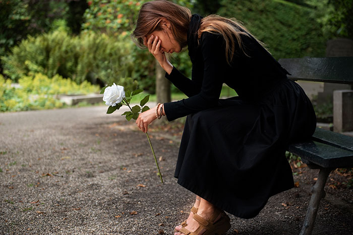 Woman sitting on park bench holding a white rose, appearing upset, reflecting on sister unwanted siblings adoption feelings. Woman sitting on park bench holding a white rose, appearing upset, reflecting on sister unwanted siblings adoption feelings.