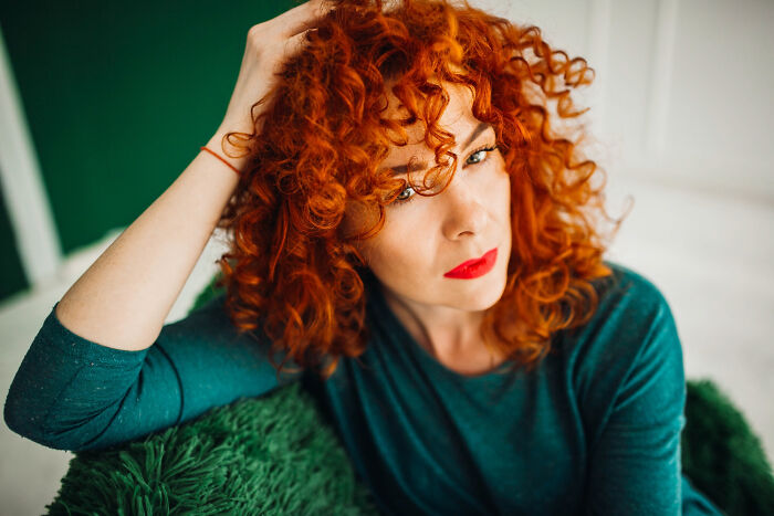 Woman with curly red hair and teal shirt looking thoughtful, reflecting on getting too short haircut and loss emotions Woman with curly red hair and teal shirt looking thoughtful, reflecting on getting too short haircut and loss emotions