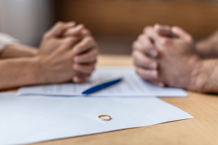 Couple with hands clasped across a table with a wedding ring on documents symbolizing shallow man’s relationship issues. Couple with hands clasped across a table with a wedding ring on documents symbolizing shallow man’s relationship issues.