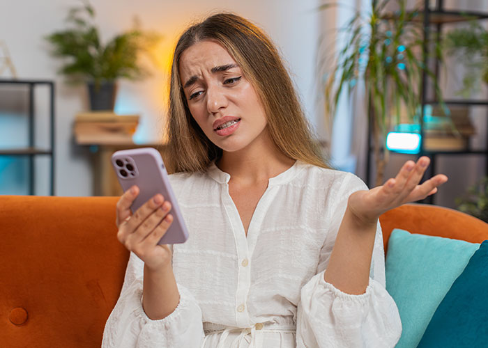 Woman upset and considering canceling friend’s holiday booking after harassment by her brother’s girlfriend, holding phone indoors. Woman upset and considering canceling friend’s holiday booking after harassment by her brother’s girlfriend, holding phone indoors.