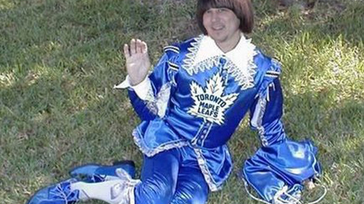 Man wearing a funny Toronto Maple Leafs uniform costume lying on grass and waving with a playful expression