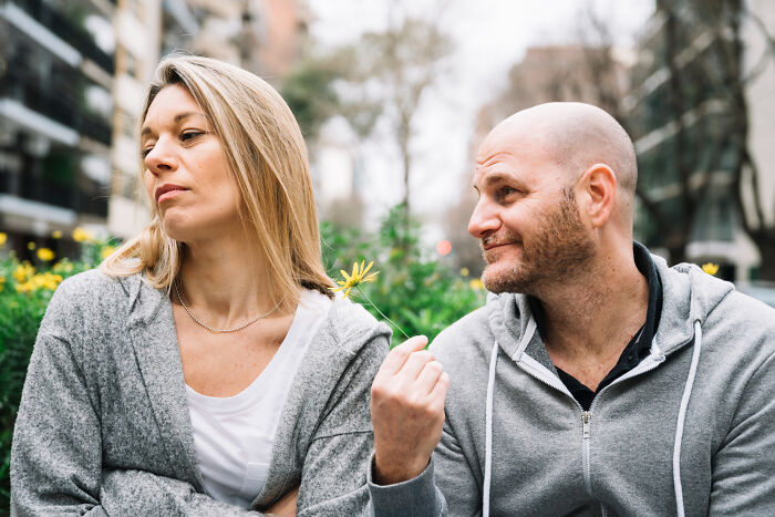 A man offering a flower to a woman who looks upset, illustrating signs of a spouse causing relationship regret.