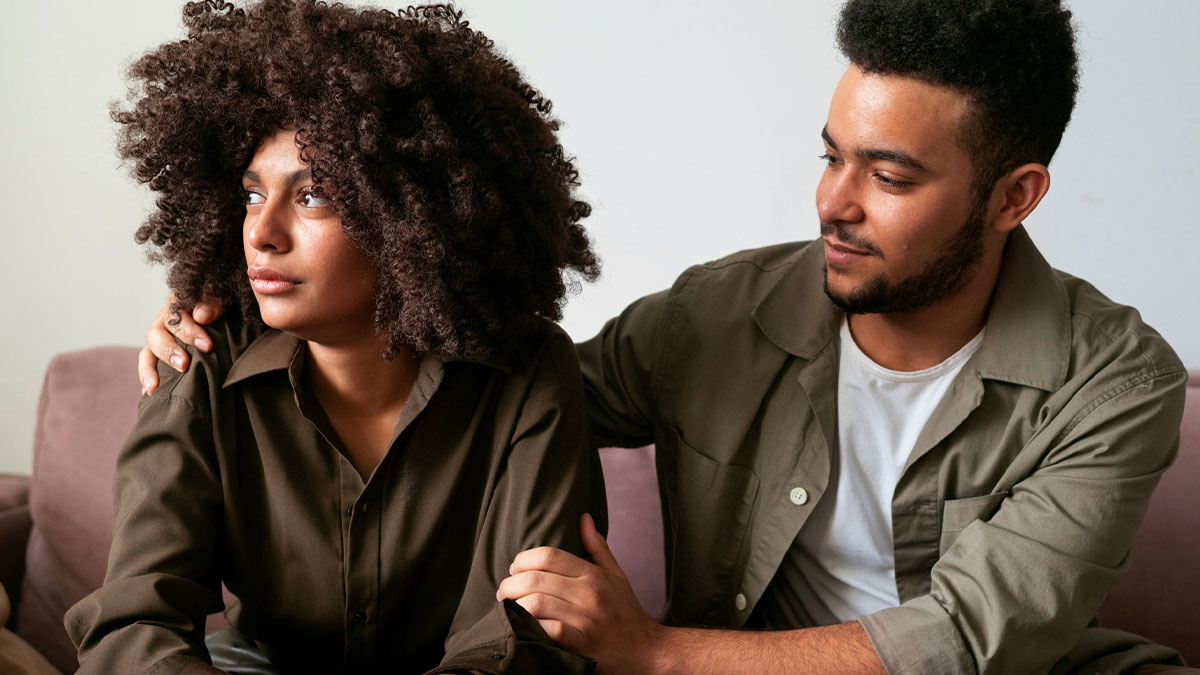 Couple having a serious conversation, woman looking away upset, man gently trying to comfort her showing signs of a possible spouse.