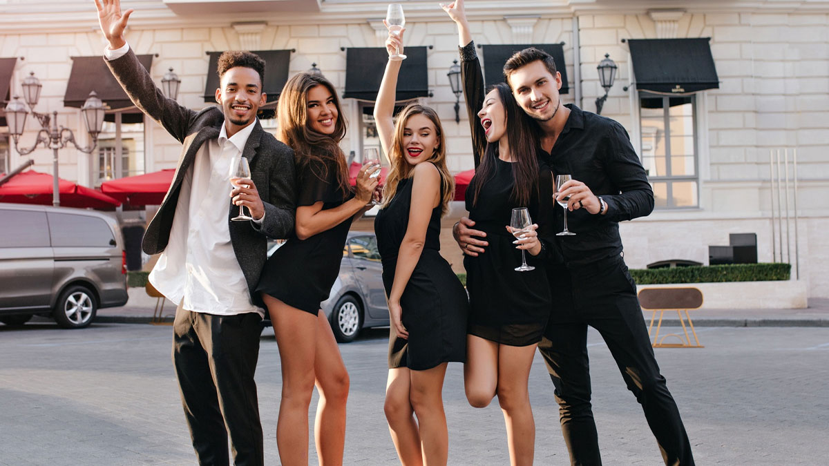 Group of friends celebrating outdoors with drinks, capturing the moment of strangers crashing a wedding photoshoot.