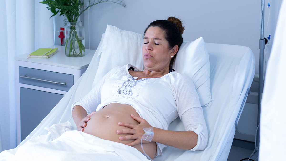 Pregnant woman in hospital bed experiencing labor pains before scheduled C-section delivery.