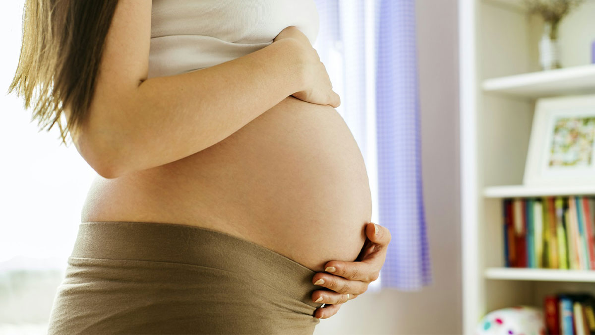 Pregnant woman gently holding her belly indoors, symbolizing pregnancy and family challenges involving husband and baby.